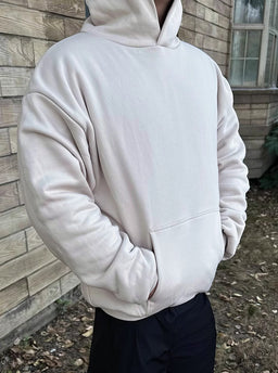 Ein Model posiert in dem beigefarbenen 800 GSM Heavyweight Hoodie von Gradualbasics.